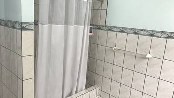 A bathroom with a shower curtain, tiled walls, and a shower control handle.