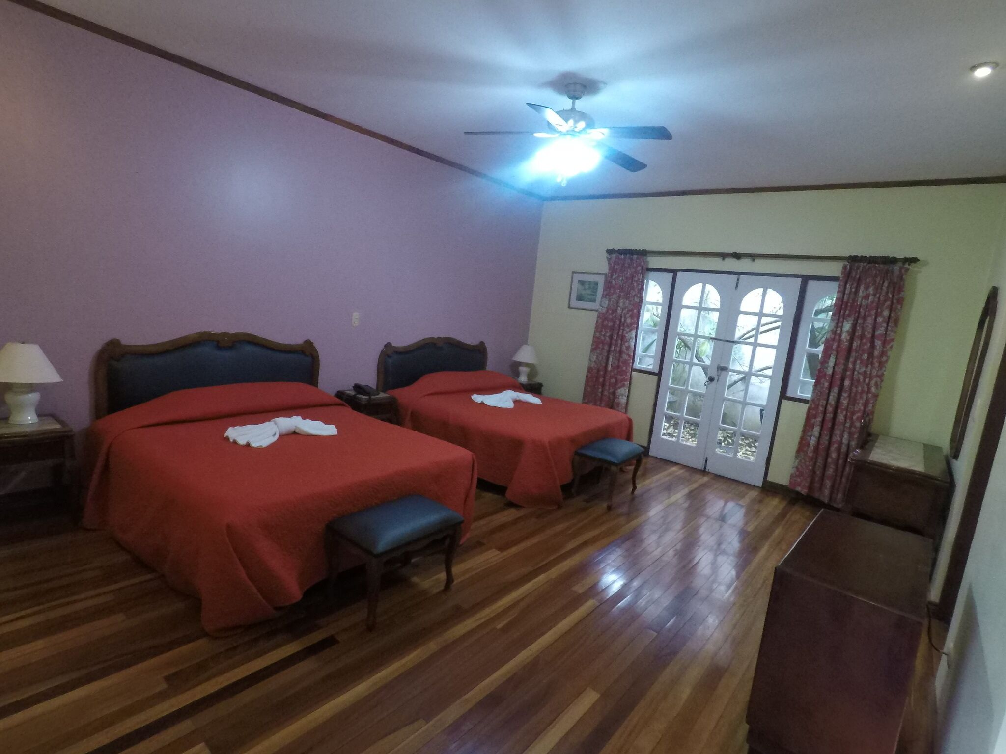 A room with two beds, wooden flooring, a ceiling fan, and a door leading outside.
