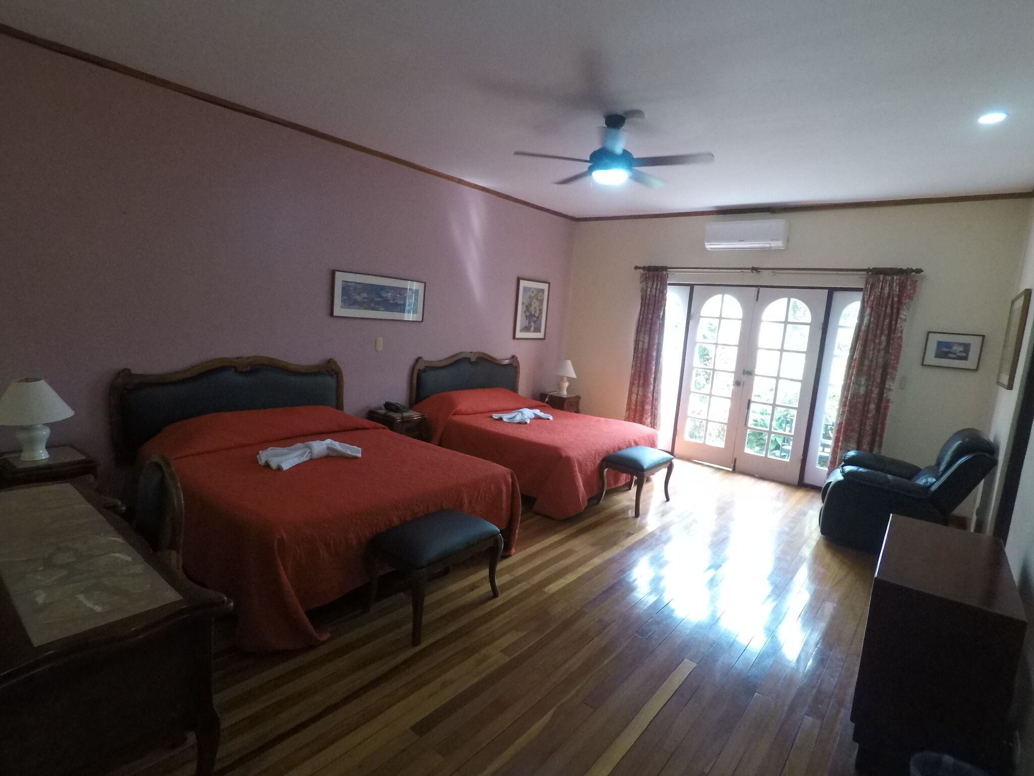 A hotel room with two beds, a ceiling fan, a desk with a lamp, and a chair.