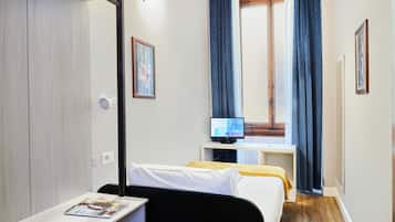 A hotel room with a bed, a desk, a television, and a window with curtains.