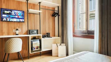 Ein modernes Hotelzimmer mit einer Holzvertäfelung, einem Flachbildfernseher, einem Schreibtisch mit Stuhl, einem Bett und einem Fenster mit Rollläden.