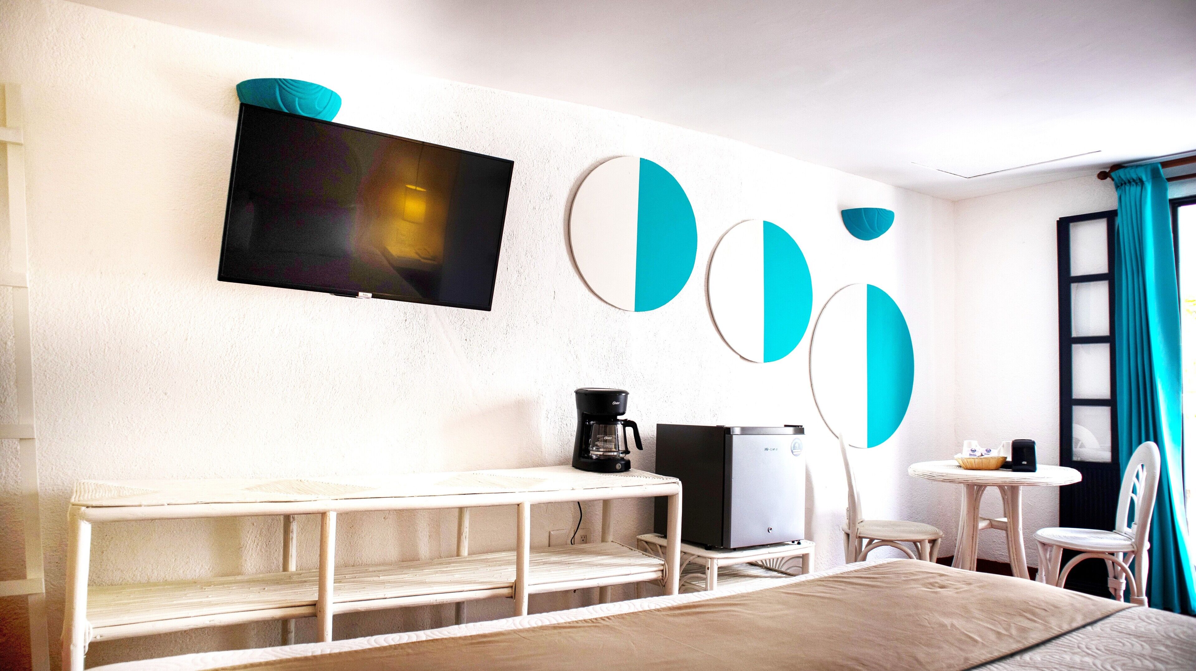 A hotel room with a bed, a TV mounted on the wall, a coffee maker, a small table with a basket, and a chair.