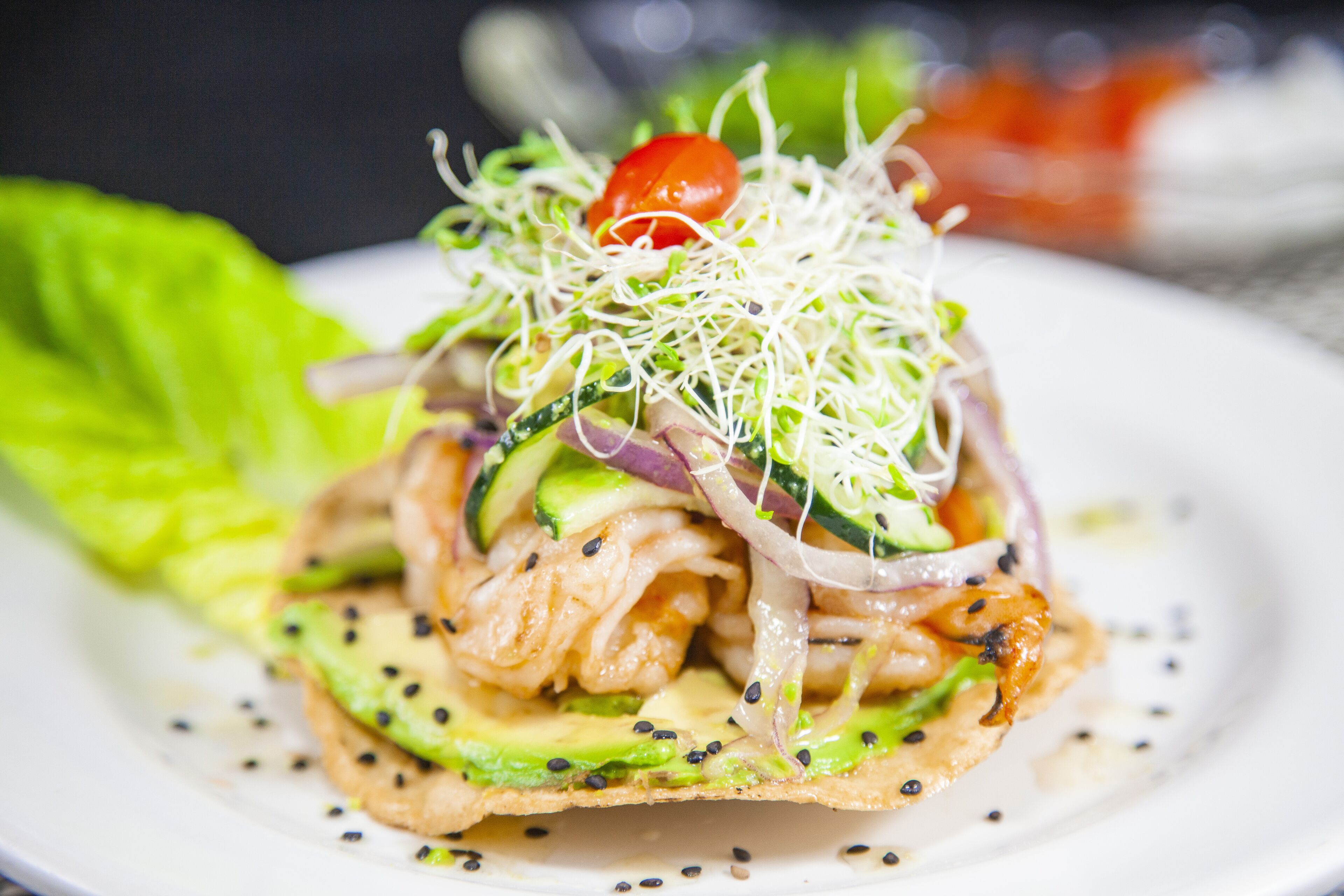 A plate of food with various ingredients including avocado, cucumber, and a cherry tomato.