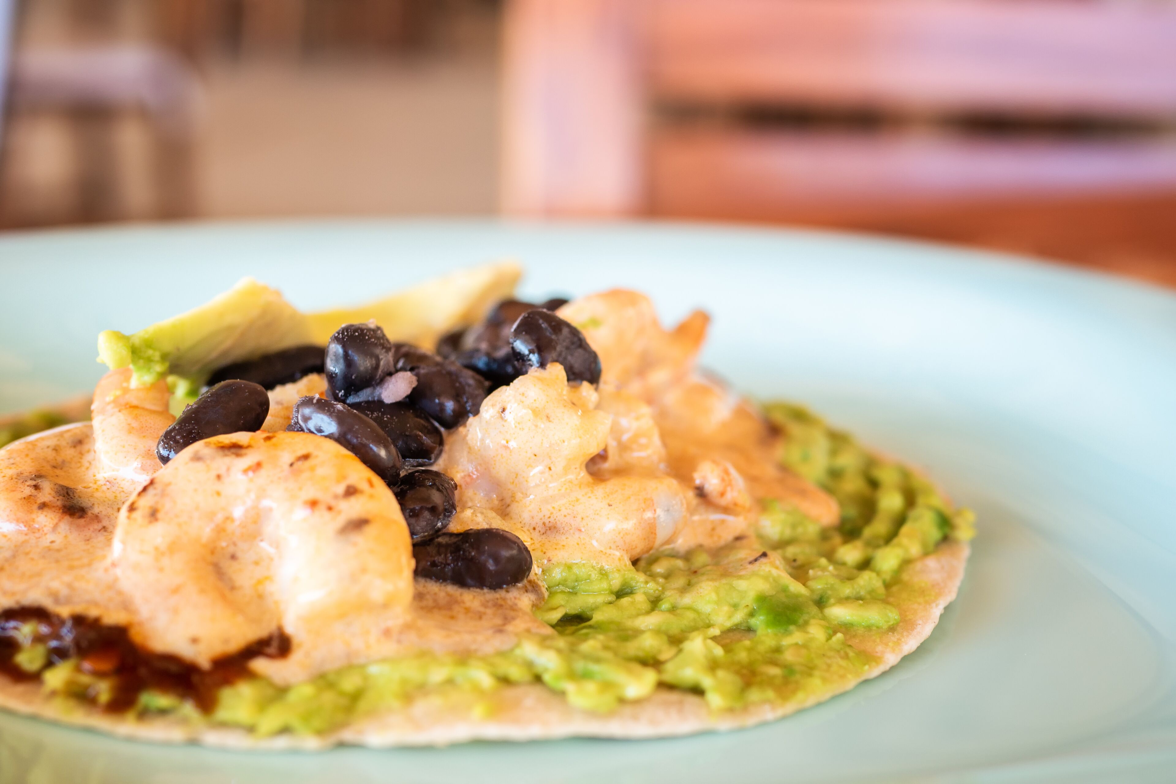 Un plato con tortilla cubierta de aguacate, frijoles negros y camarones.