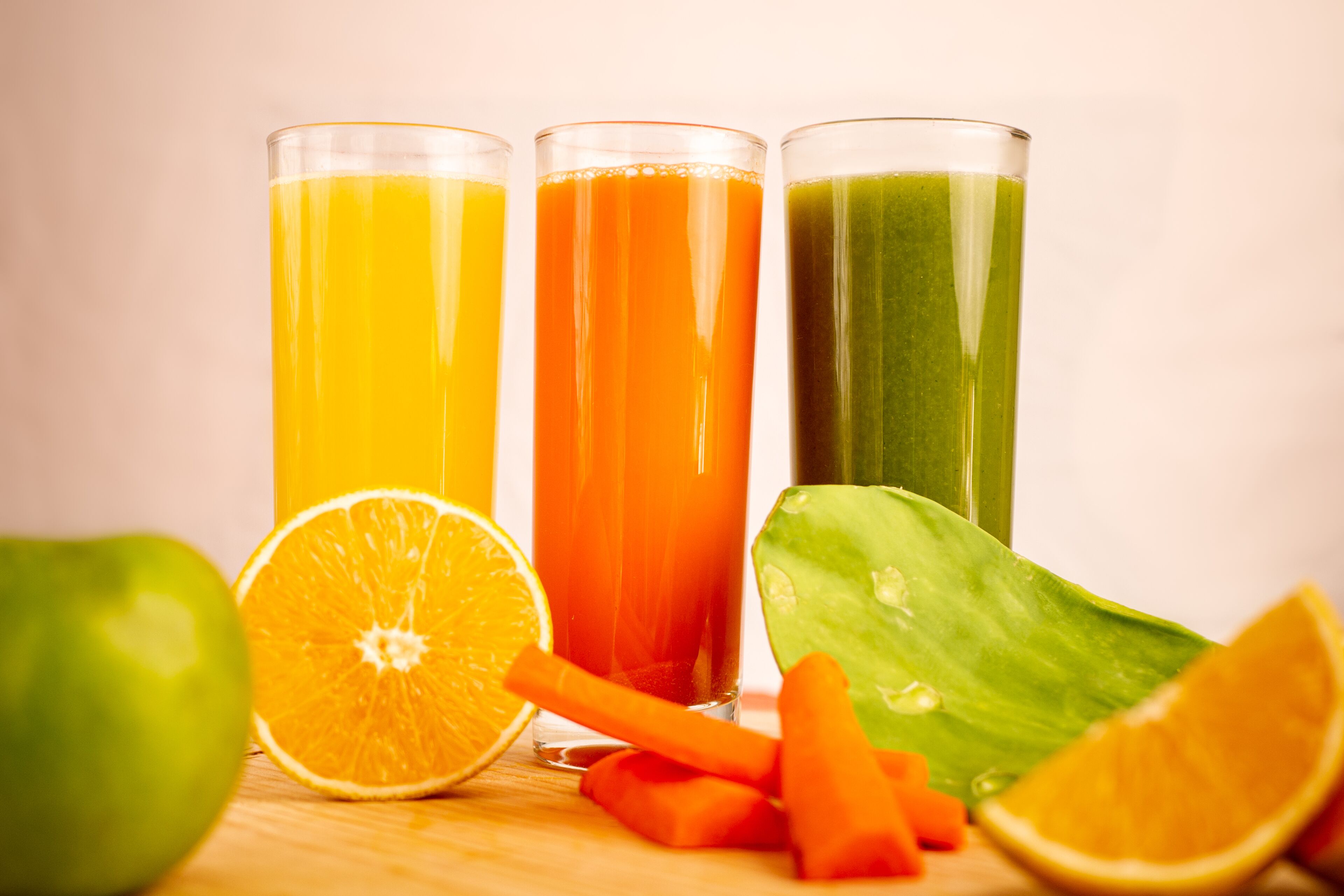Tre glas juice, en apelsinskiva och några morotsstavar på en träyta.