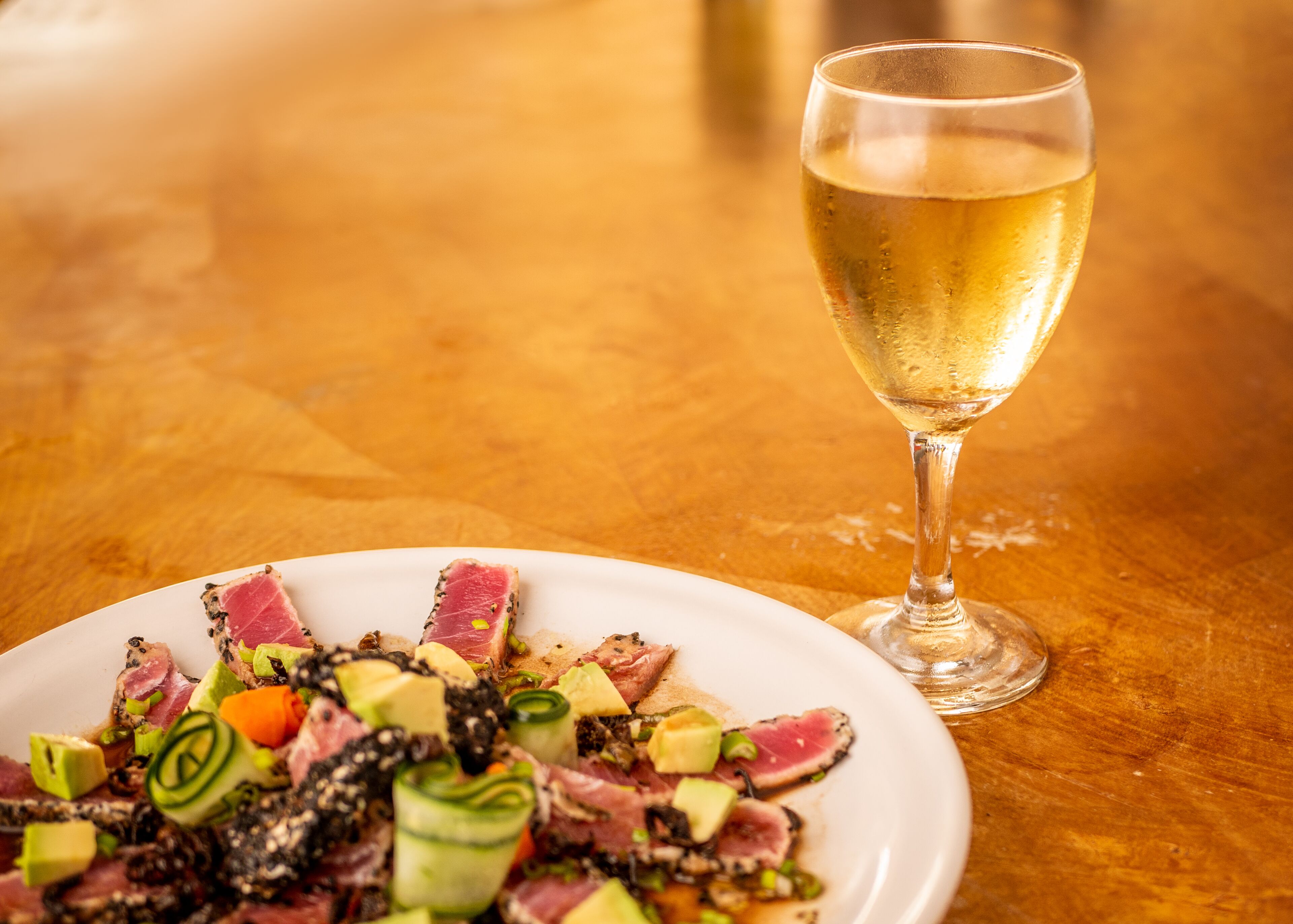 A plate of food with various ingredients and a glass of white wine on a wooden table.