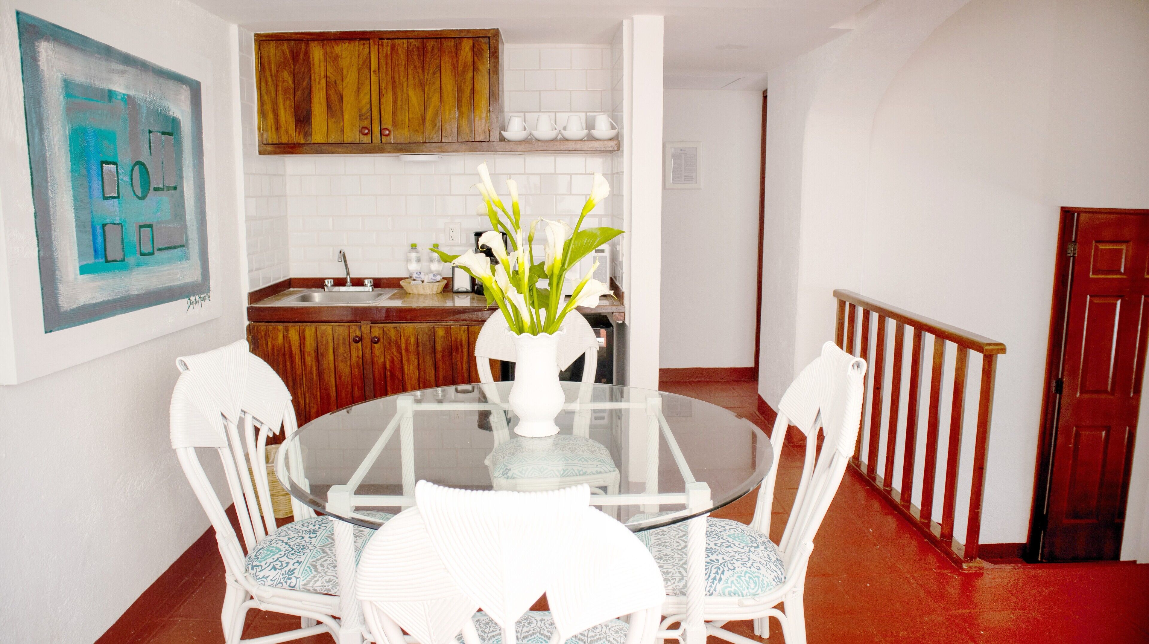 A dining area with a glass table surrounded by white chairs, a white vase with flowers, and wooden cabinets above.