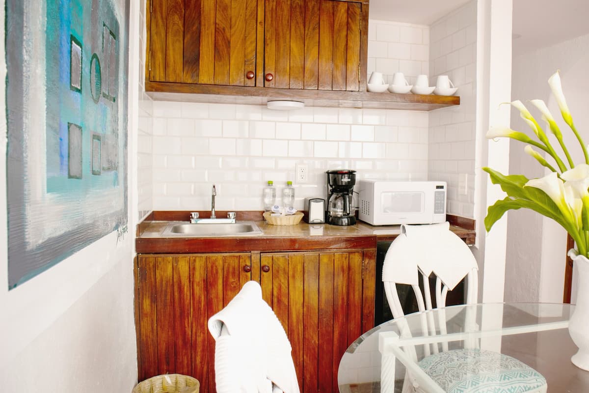 Een keuken met houten kastjes, een witte betegelde spatwand, een magnetron, een koffiezetapparaat en een vaas met witte bloemen op een tafel.