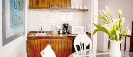 A kitchen with wooden cabinets, a white tiled backsplash, a microwave, a coffee maker, and a vase with white flowers on a table.