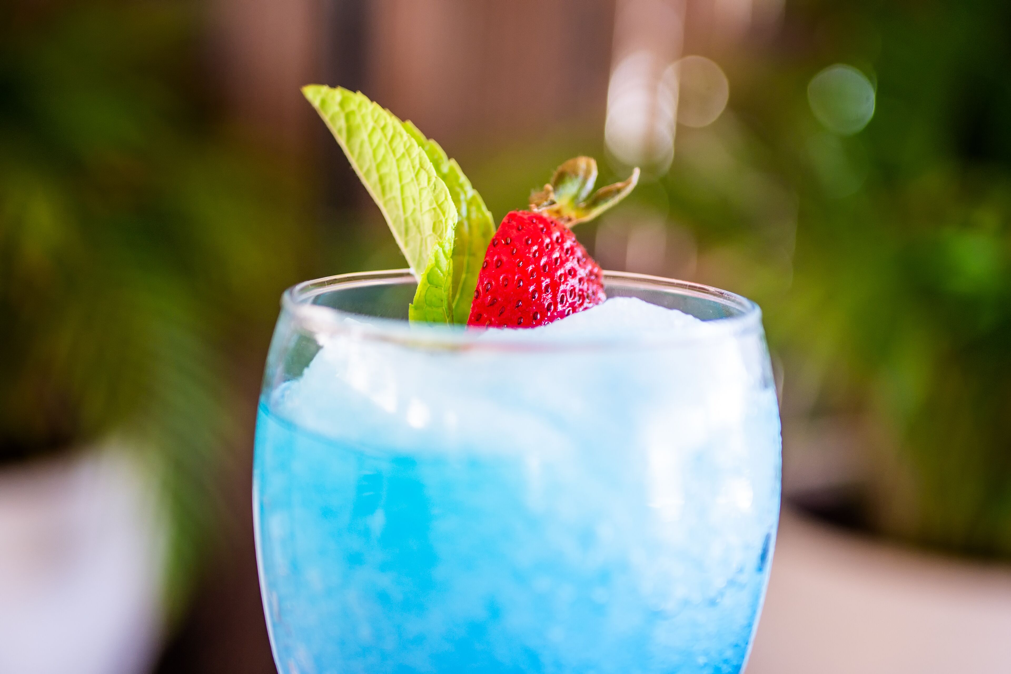 Un verre contenant un liquide bleu, une fraise et une feuille de menthe.