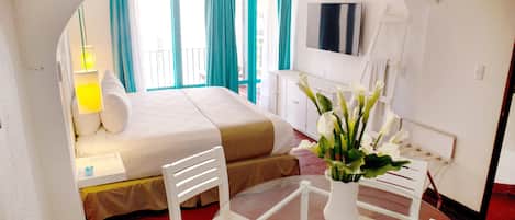 Habitación de hotel con cama, escritorio, silla, televisor y un florero con flores.