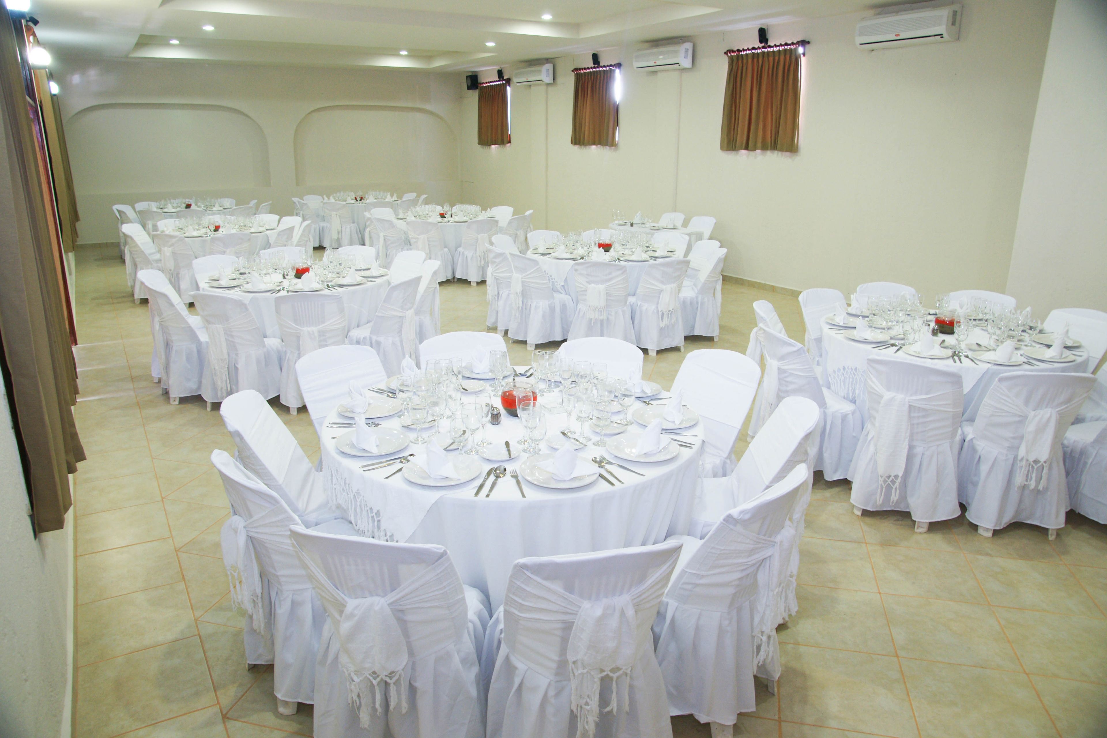 A banquet hall with multiple round tables set for dining, each with white tablecloths and matching chairs.