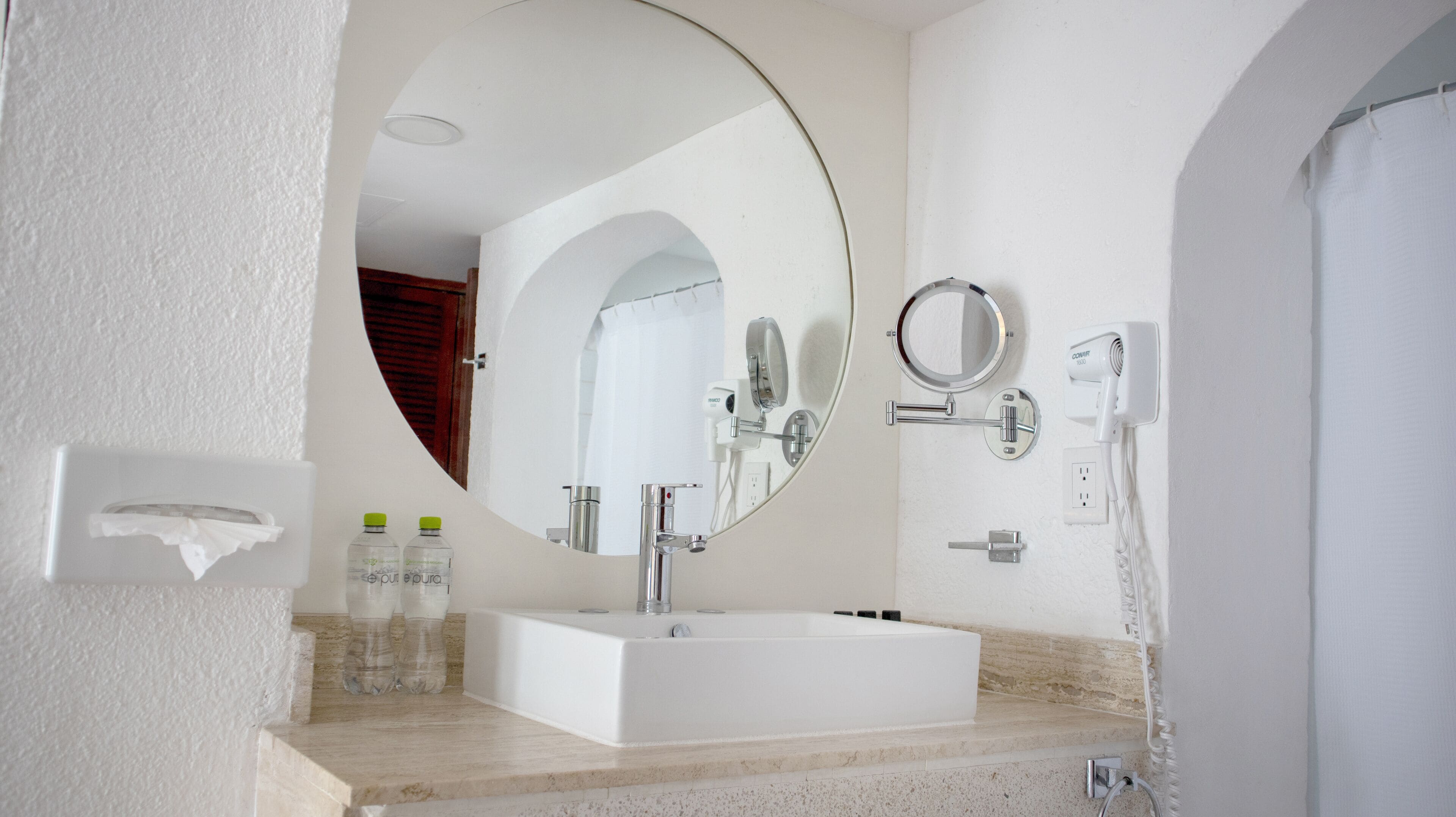 Een moderne badkamer met een witte wastafel, een grote spiegel, een handdouche en een zeepdispenser.