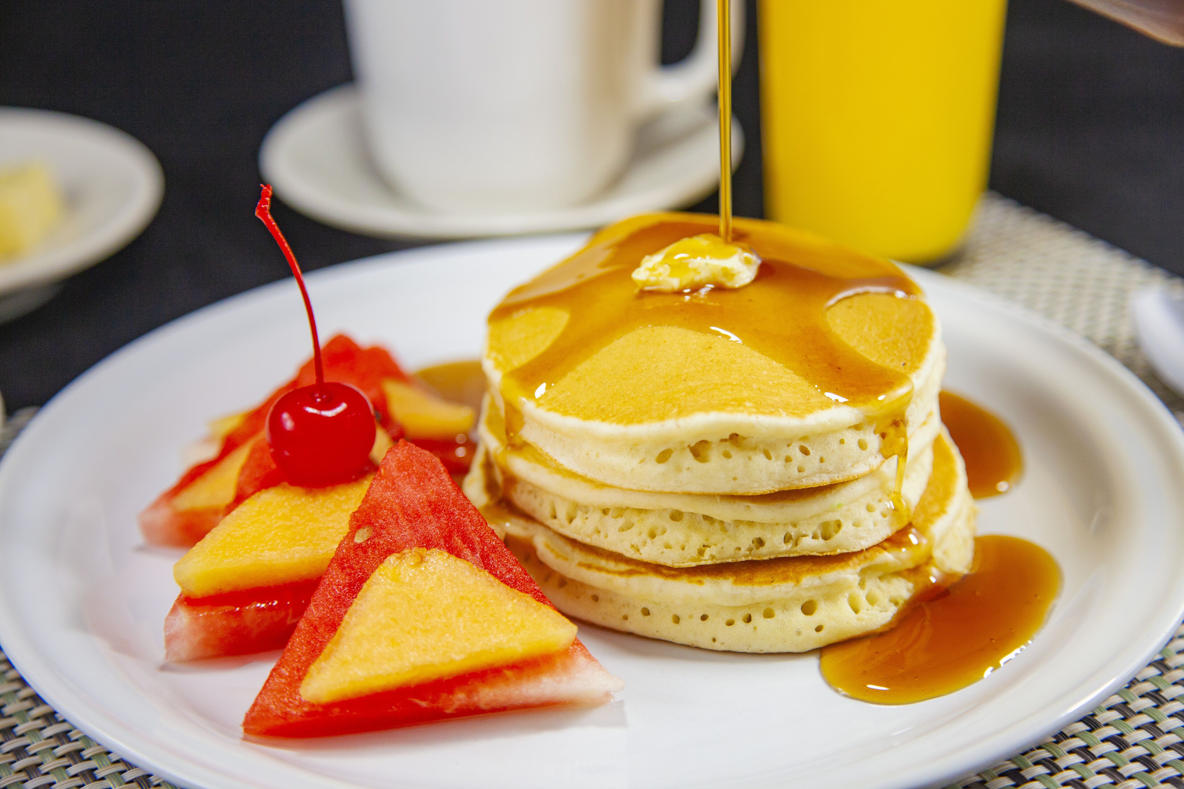 A plate of pancakes with syrup and fruit slices.