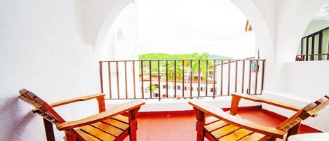 A balcony with two wooden chairs and a white sofa, overlooking a green landscape.