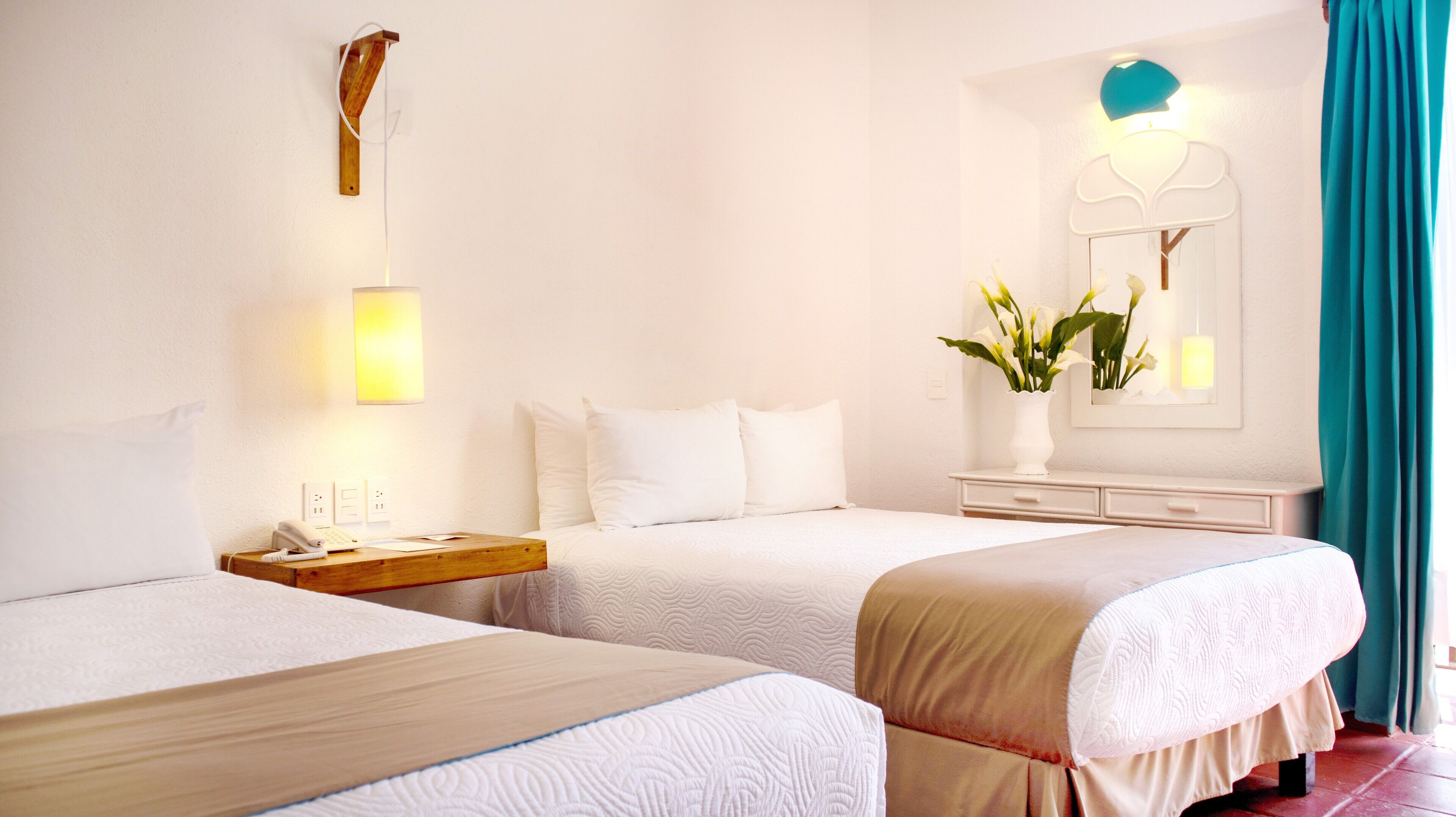 Een hotelkamer met twee bedden, een nachtkastje met een lamp, een dressoir en een spiegel met decoratieve lijst.