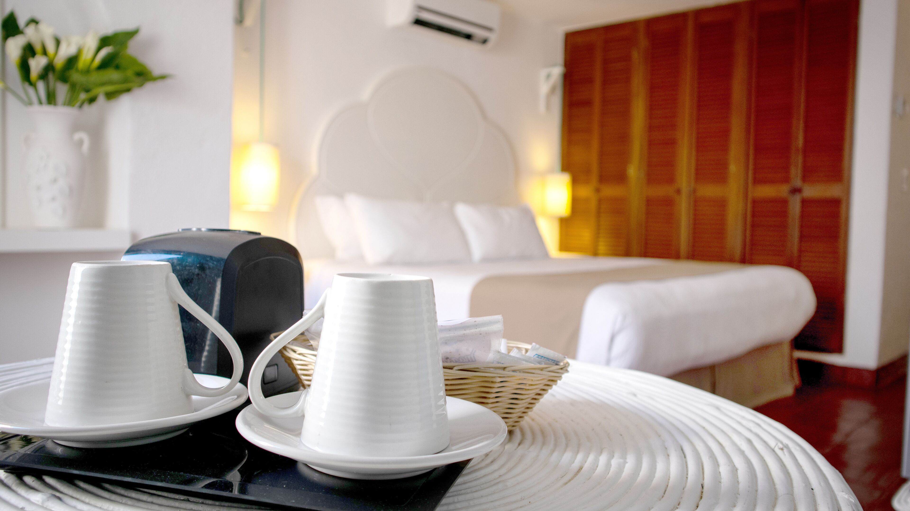 Ein Hotelzimmer mit einem Bett, einem weißen Kopfstützen, einem Nachttisch mit Lampe und einem Korbwäscheschrank.