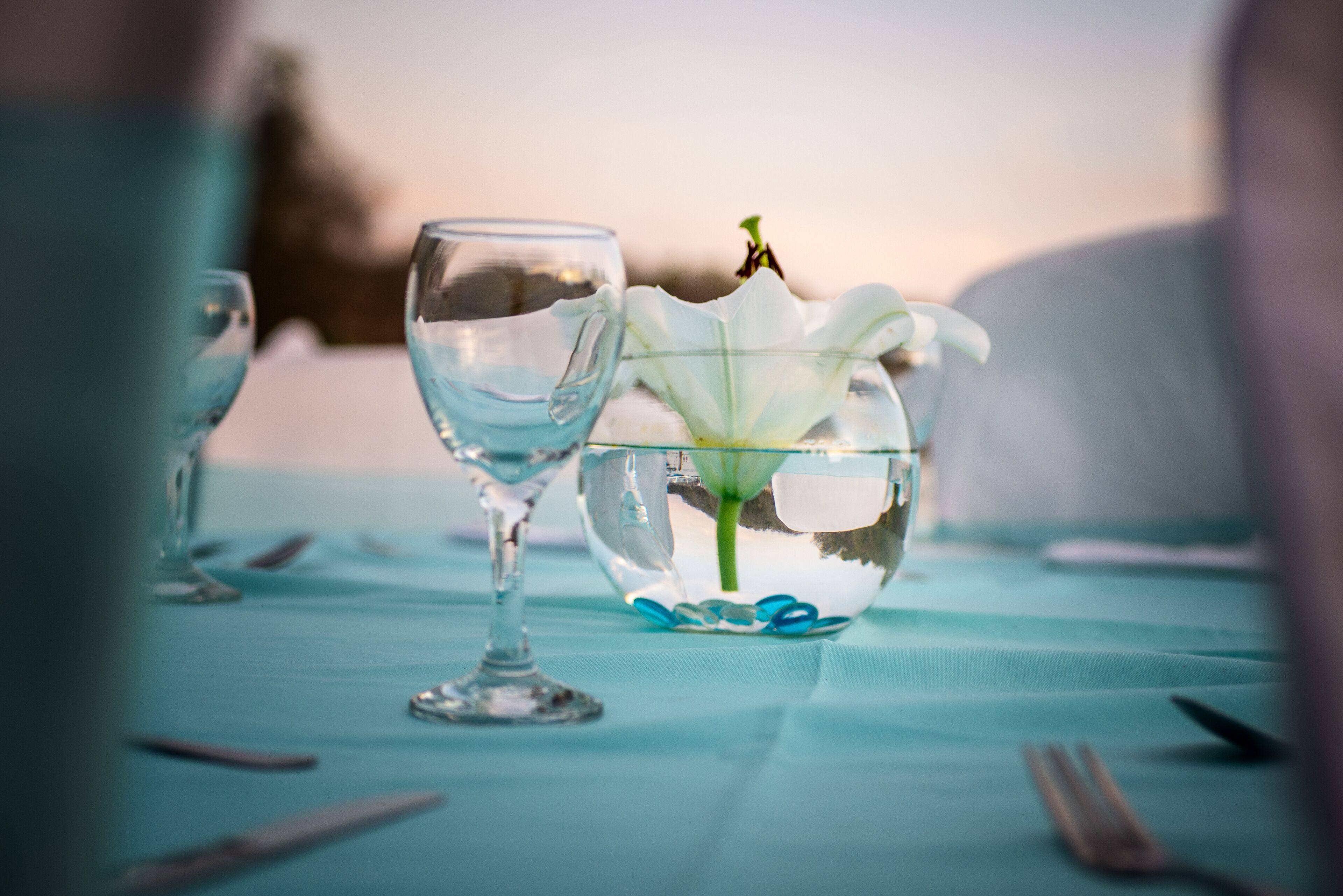 Ein Tisch, gedeckt mit einer Schale aus Glas mit einer weißen Blüte, einem Glas und Besteck.