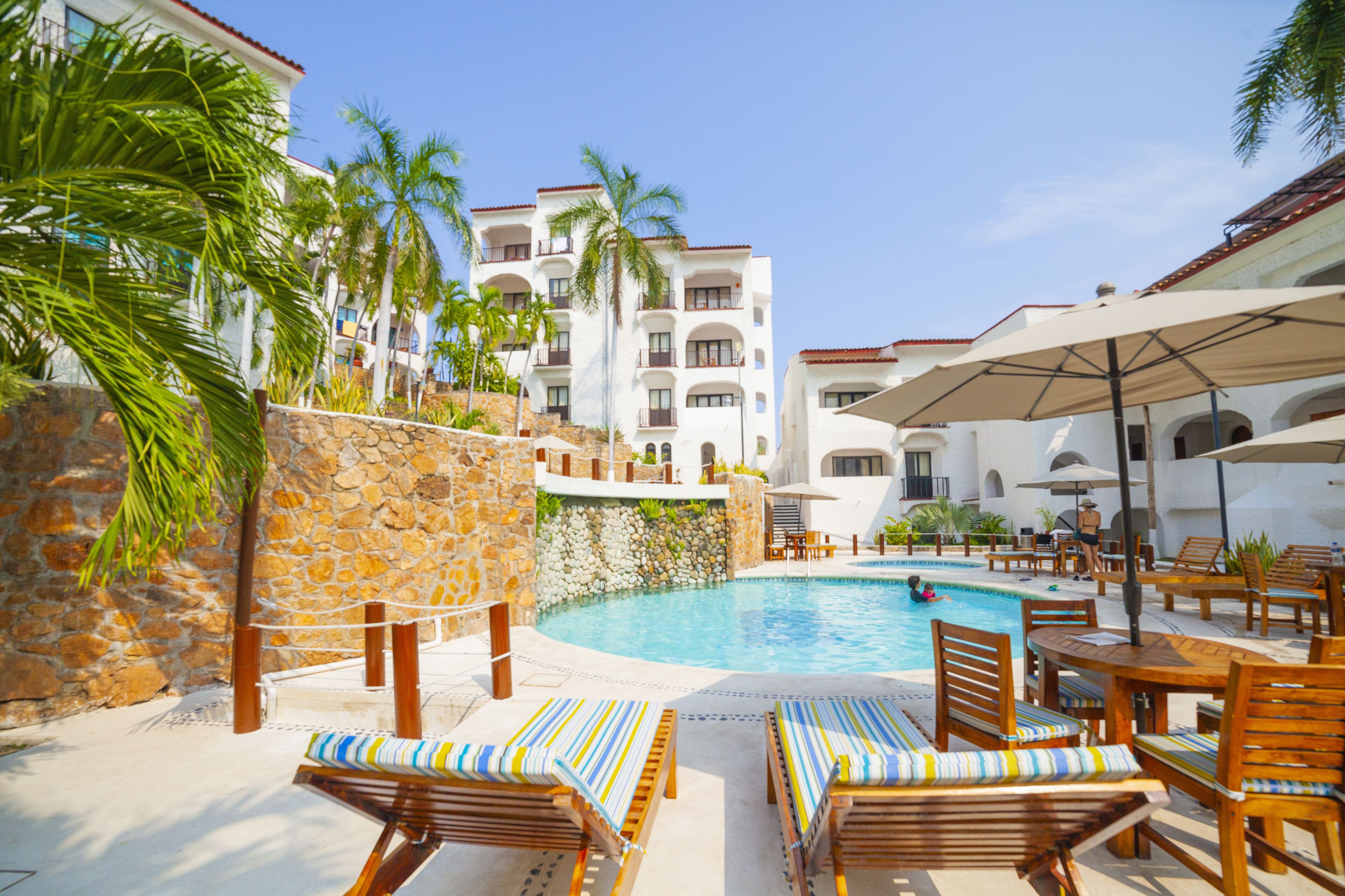 A poolside area with lounge chairs, a swimming pool, and a stone wall.