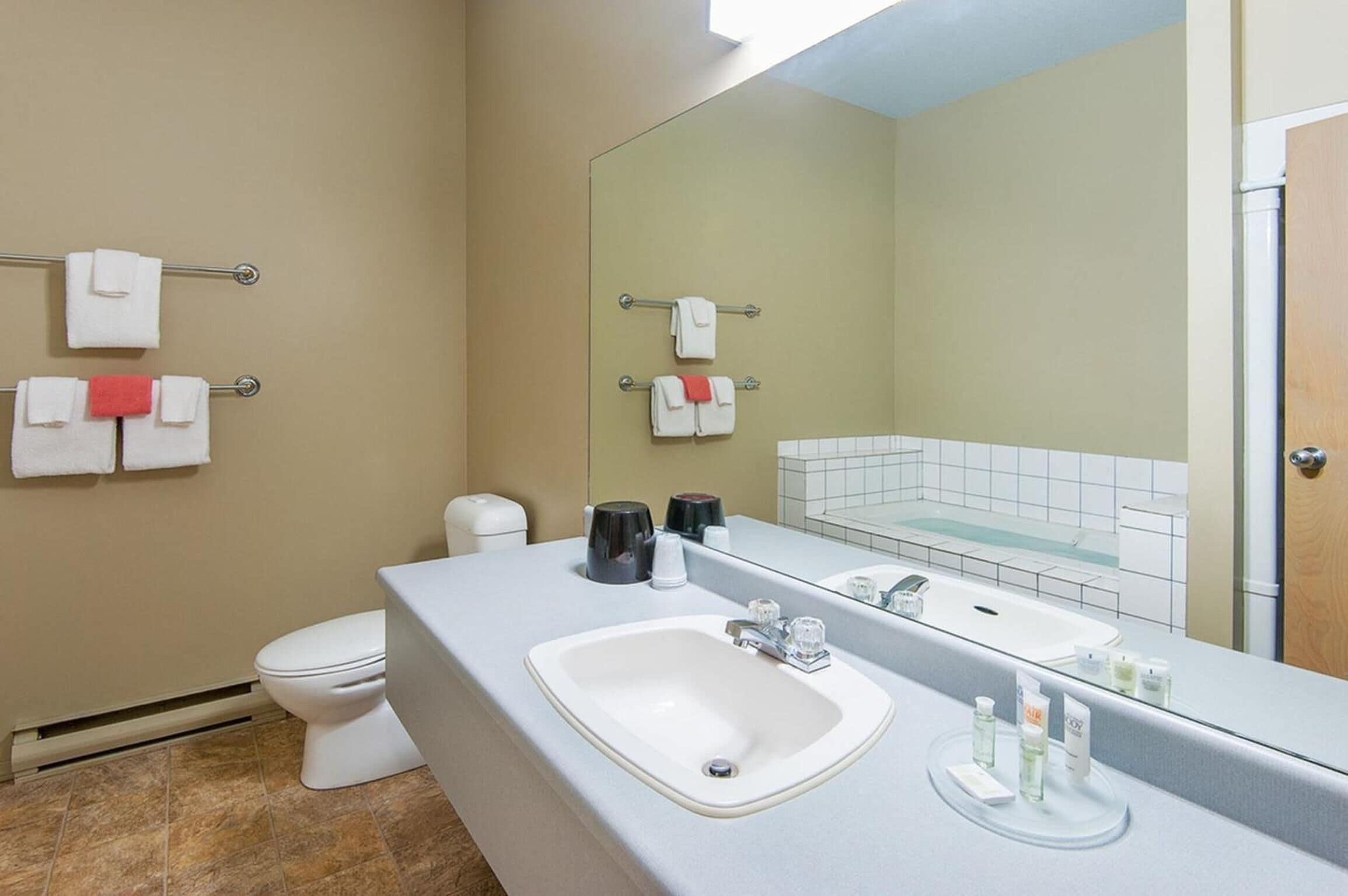 Une salle de bain moderne avec un lavabo blanc, un grand miroir et des toilettes. On y trouve des serviettes sur des porte-serviettes et des articles de toilette sur le lavabo.