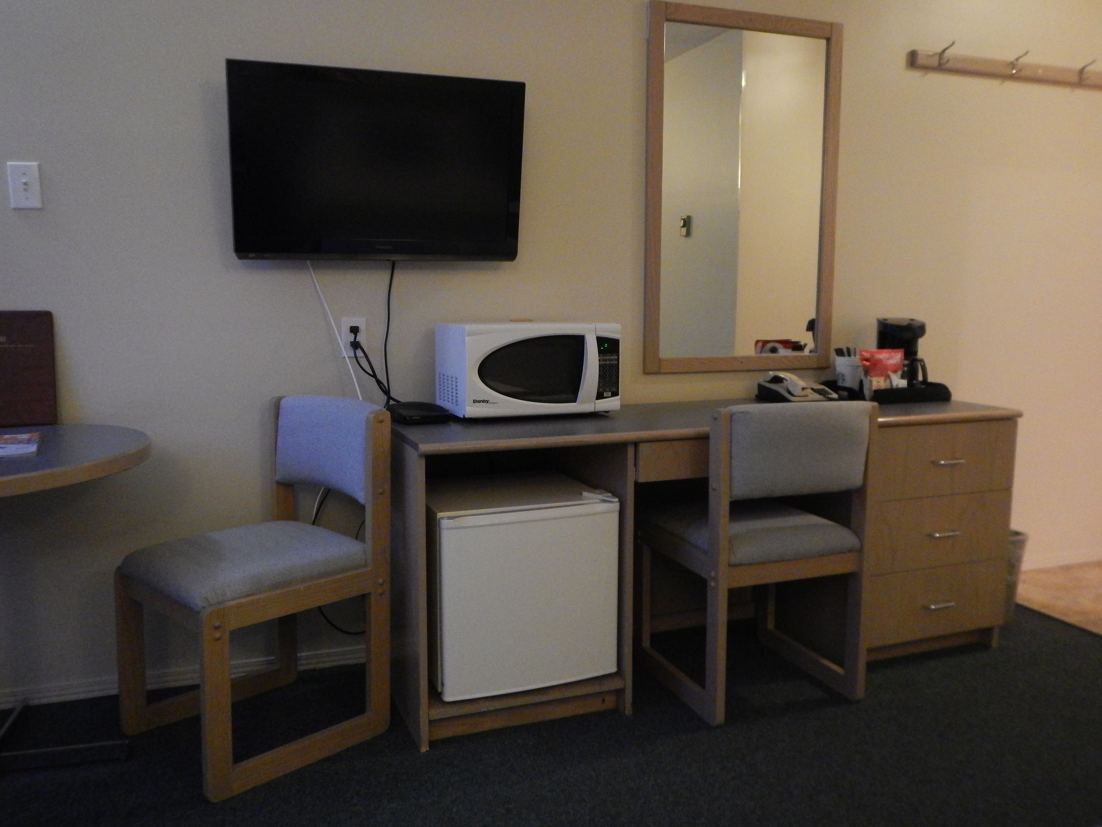 A compact hotel room with a desk, a microwave, a television, a small refrigerator, a chair, a mirror, and a cabinet.
