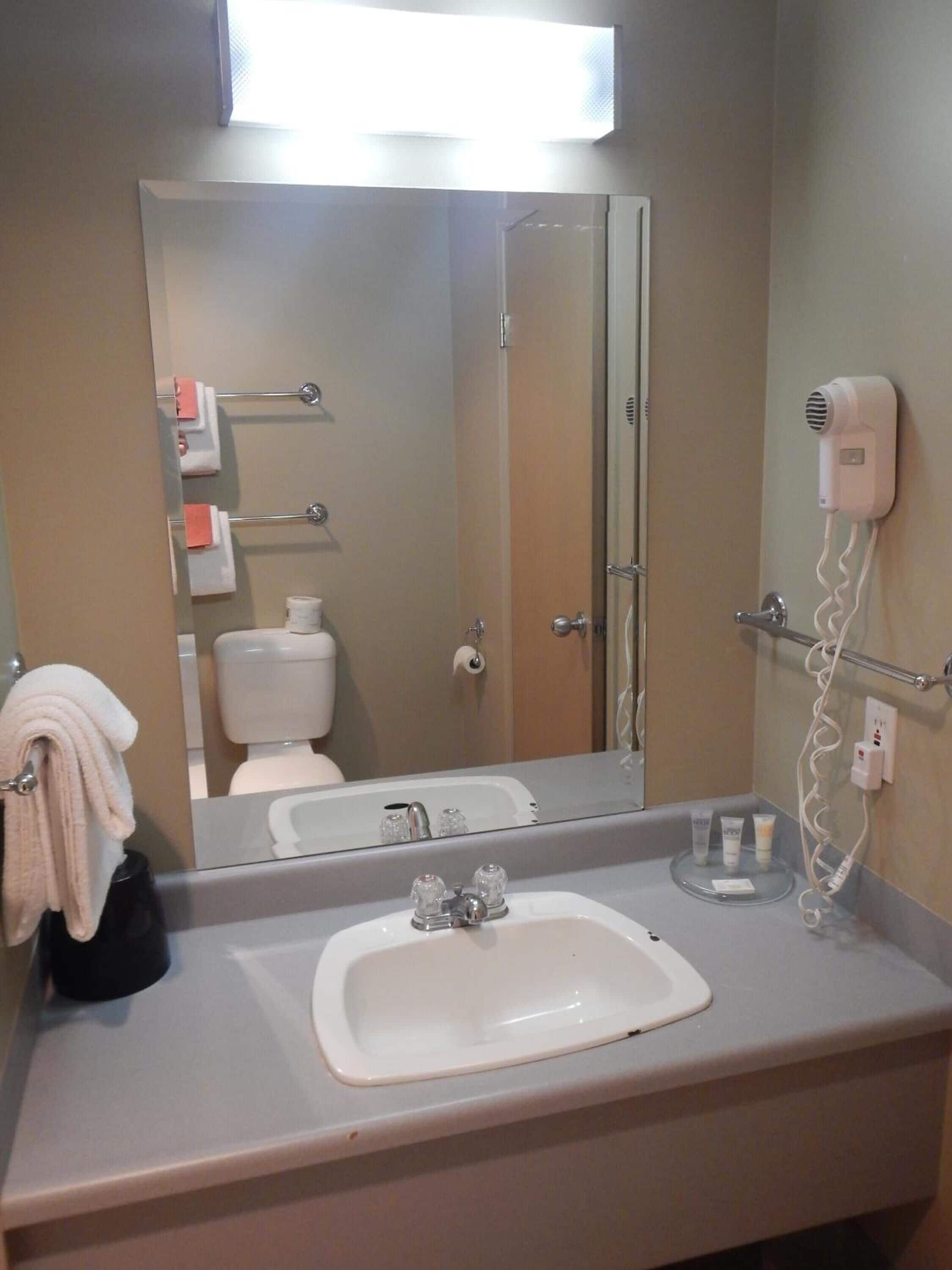 Une salle de bain équipée d’un lavabo, d’un miroir, d’un porte-serviettes et d’un sèche-cheveux.