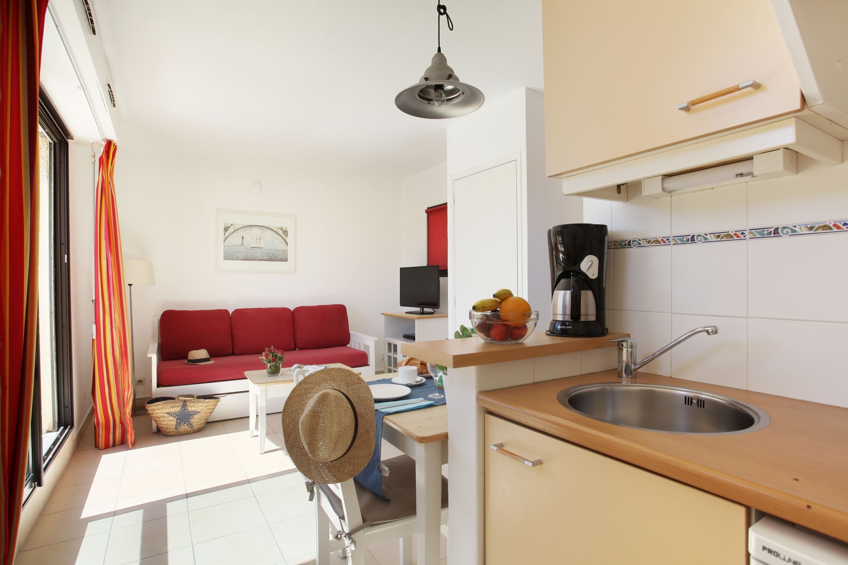 Un espace de vie compact comprenant un coin cuisine, un canapé rouge, un téléviseur et un coin repas avec une table et des chaises.