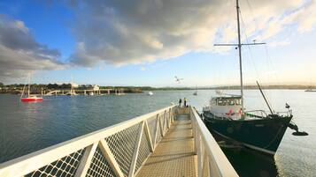 A pier with a boat docked on the right, a red boat in the water, and a person walking on the pier.