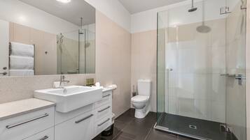 Un baño moderno con ducha de vidrio, un lavamanos blanco y un inodoro.