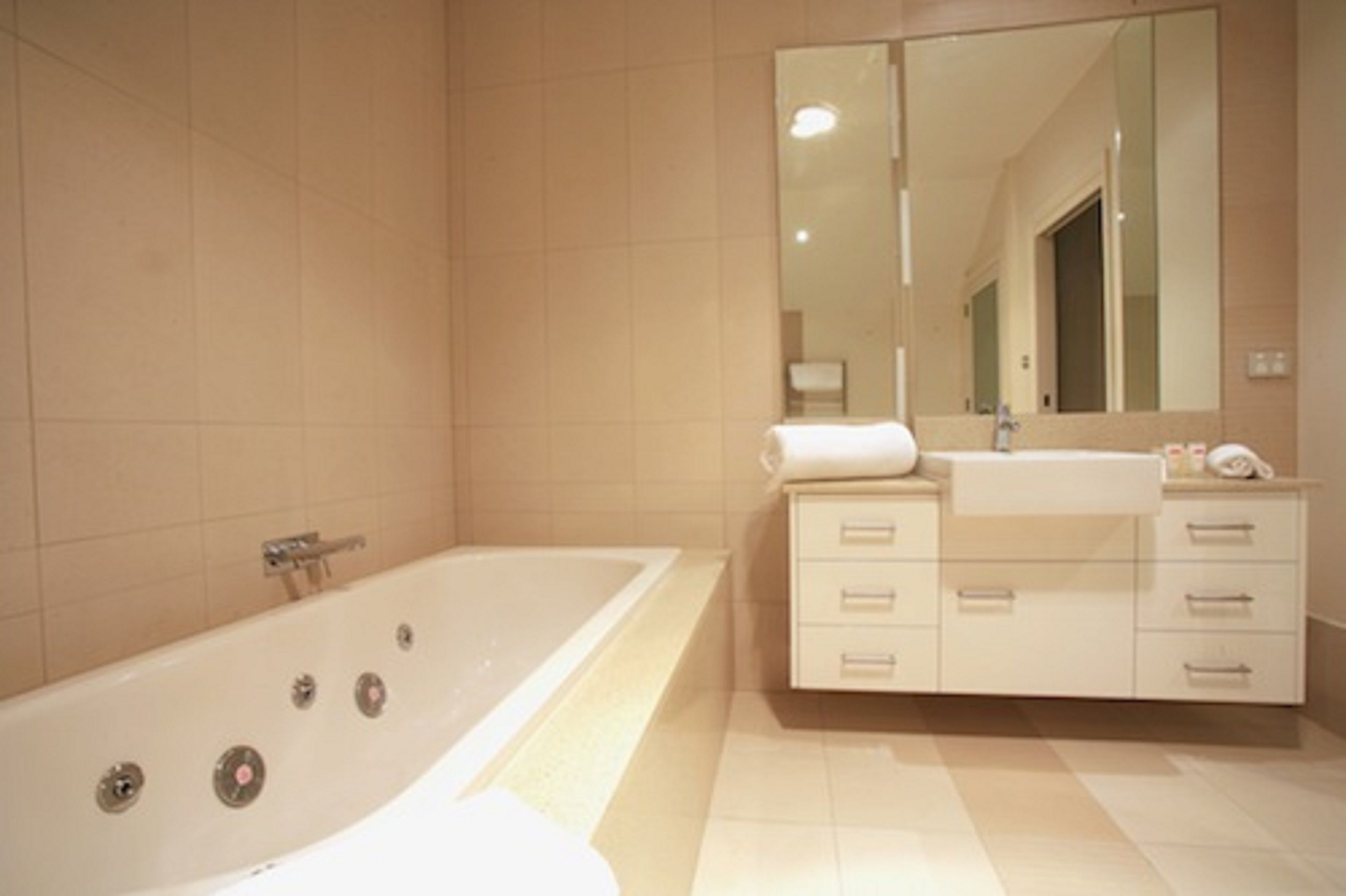Un baño moderno con una bañera grande, un tocador con cajones y un espejo.