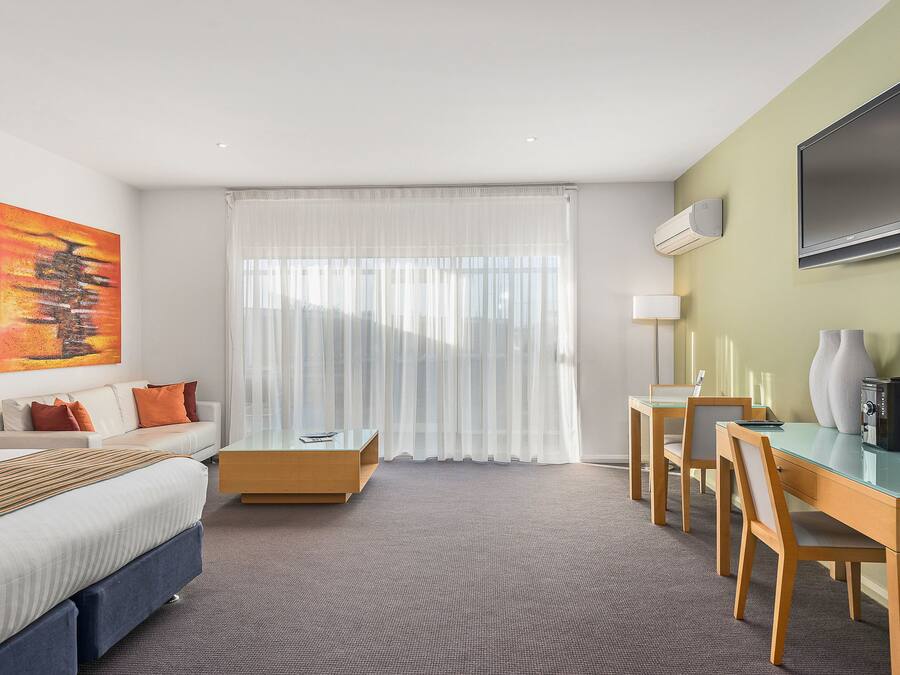 A hotel room with a bed, a desk, a chair, a TV, and a painting on the wall.