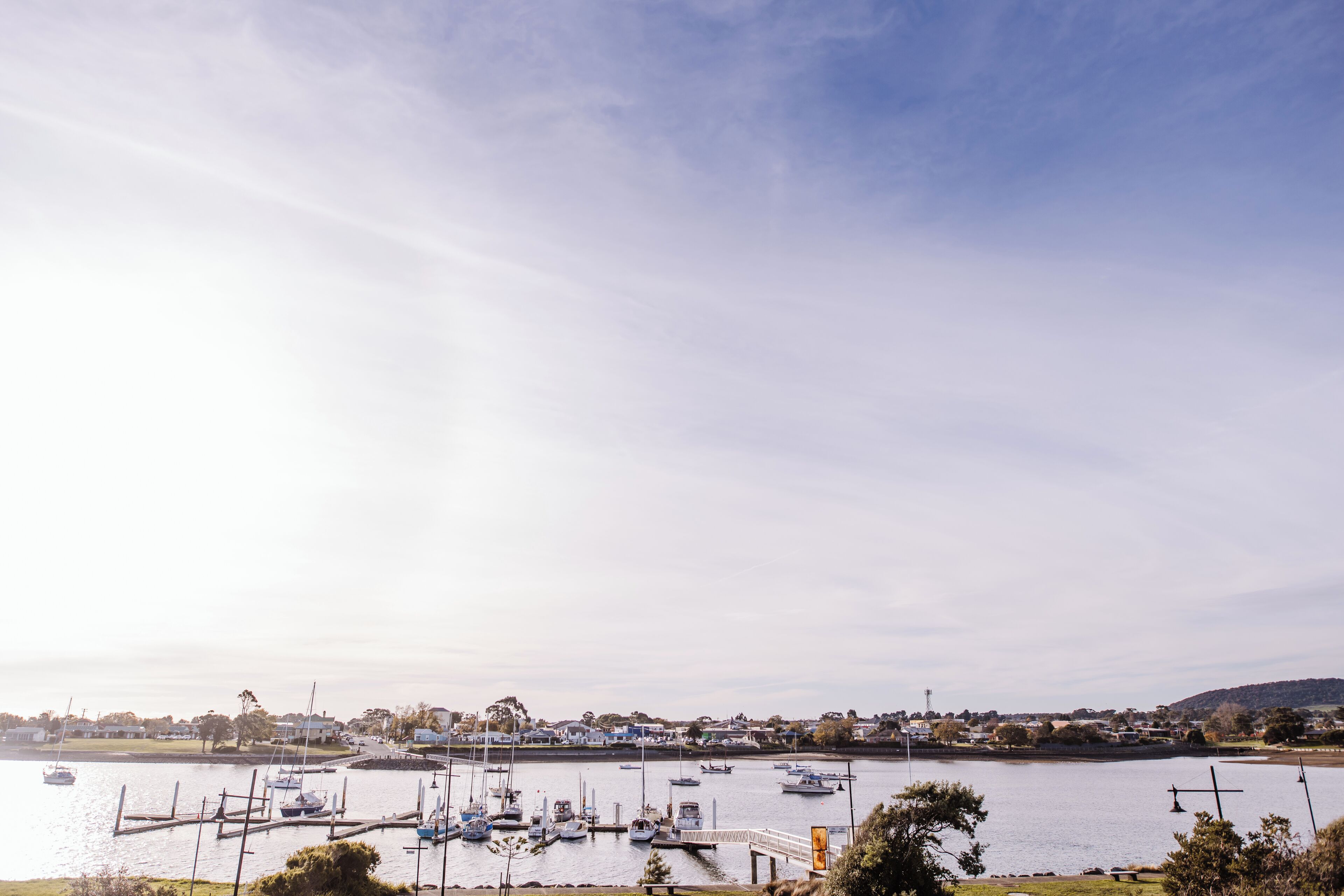 A marina with boats docked at the pier, a clear sky, and a distant town.