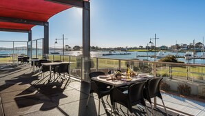 Une terrasse dotée de tables et de chaises, offrant une vue sur une marina et ses bateaux.