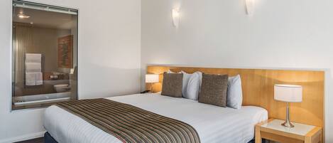 Habitación de hotel con una cama grande, cabecera de madera, dos lámparas de noche y un espejo en la pared.