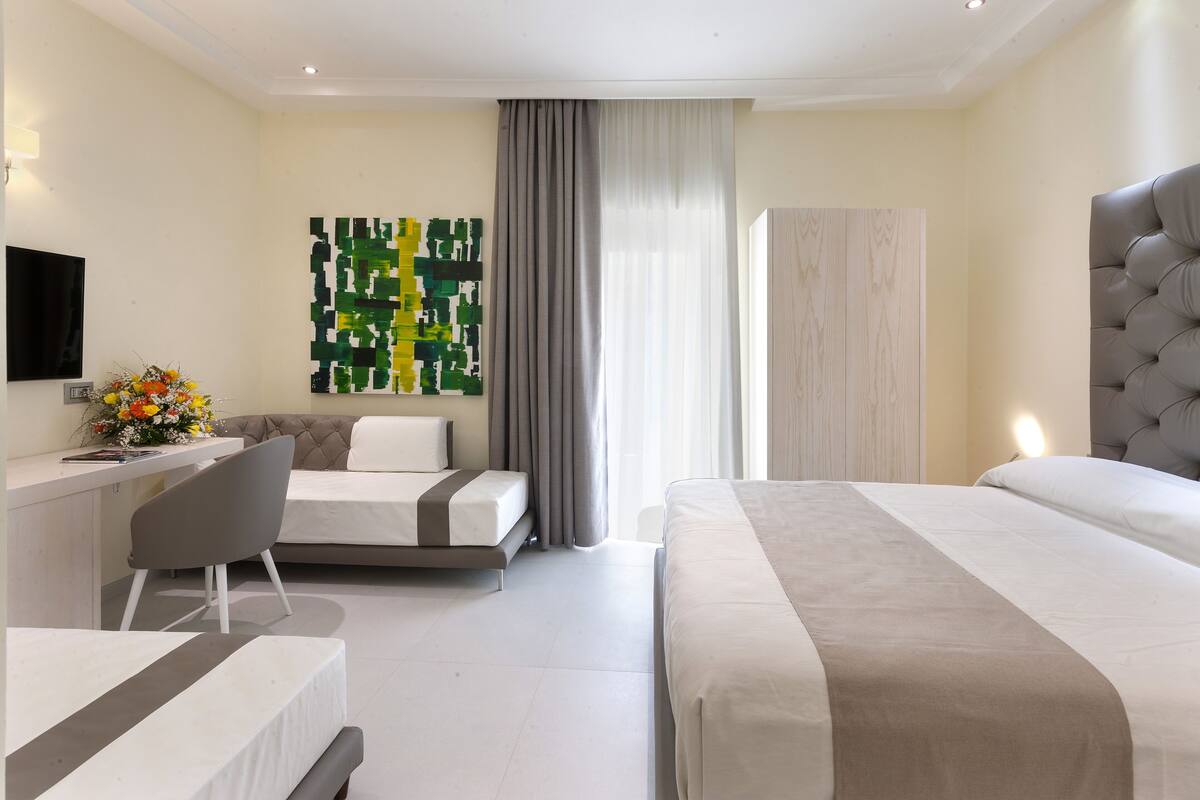 Ett modernt hotellrum med en stor säng, ett skrivbord med en stol, en platt-TV och en dekorativ väggdekoration.