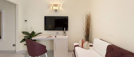 A modern hotel room with a desk, a flat-screen TV, a sofa, and a potted plant.