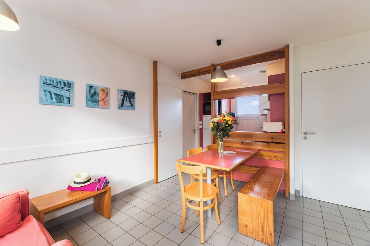 A dining area with a wooden table and chairs, a bench, and a wall with three framed pictures.