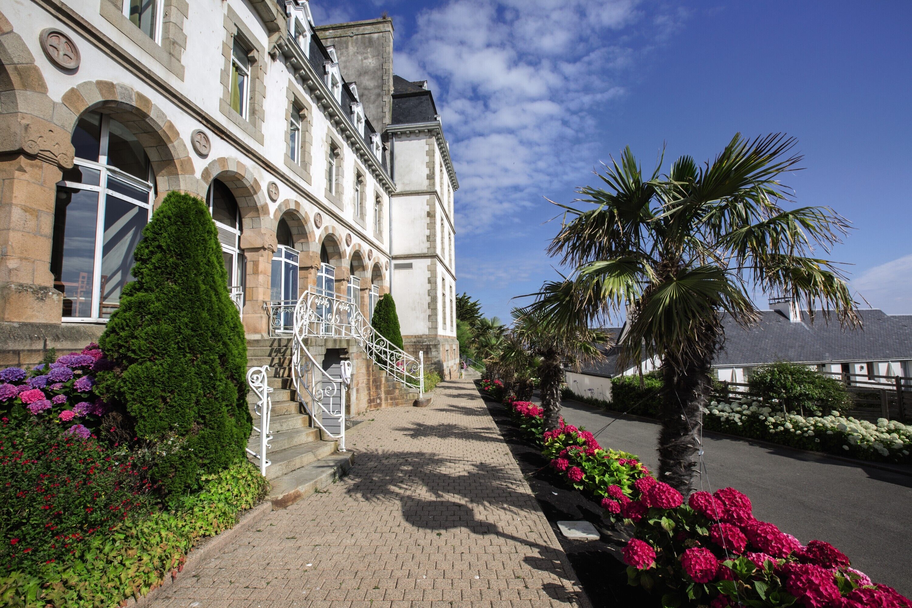 Un bâtiment historique doté d’un chemin piétonnier pavé, d’un escalier et d’une grande variété de plantes et de fleurs.