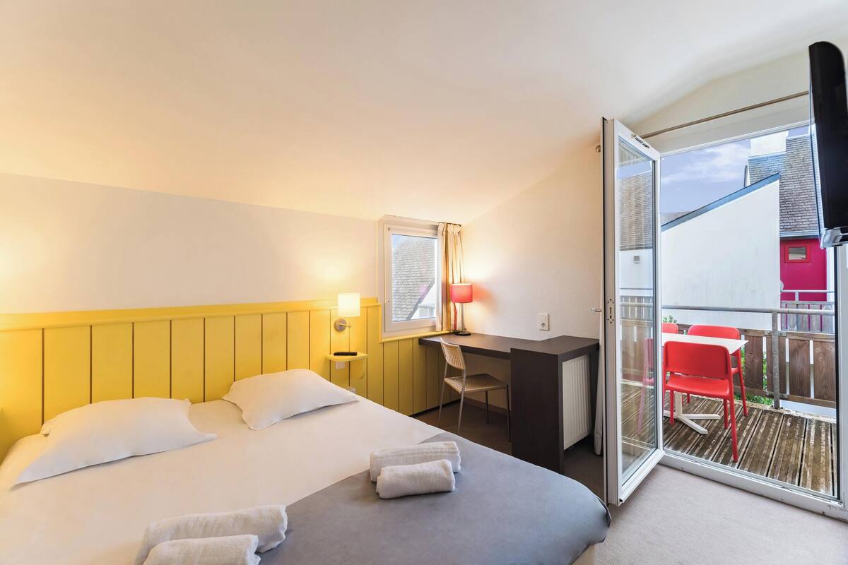 A hotel room with a bed, a desk, a chair, and a balcony with a table and chairs.