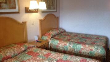 Una habitación de hotel con dos camas, cada una con cubrecama acolchado, cabecera de madera y mesita de noche con lámpara.