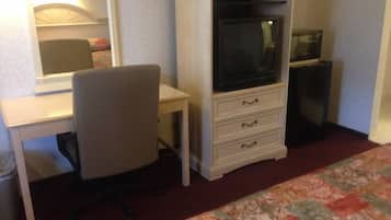 A hotel room with a bed, a desk with a chair, a television, and a trash bin.