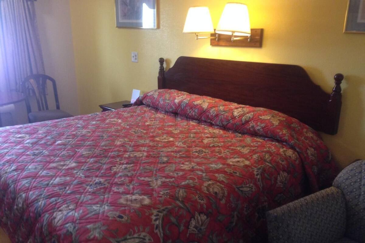 A hotel room with a large bed, a wooden headboard, two wall-mounted lamps, and a chair.