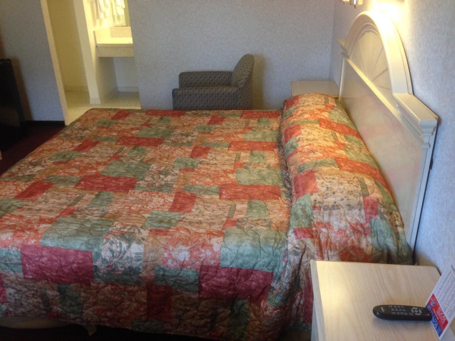 Una habitación de hotel con cama, una silla, mesita de noche y control remoto.