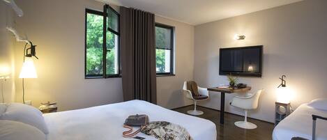 A hotel room with a bed, a desk, two chairs, a TV, and a lamp.