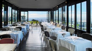 A restaurant with multiple tables set for dining, large windows offering a city view, and a balcony with a table. - L'Ermitage Hôtel Cuisine-à-Manger (Saint-Cyr-au-Mont-d'Or)