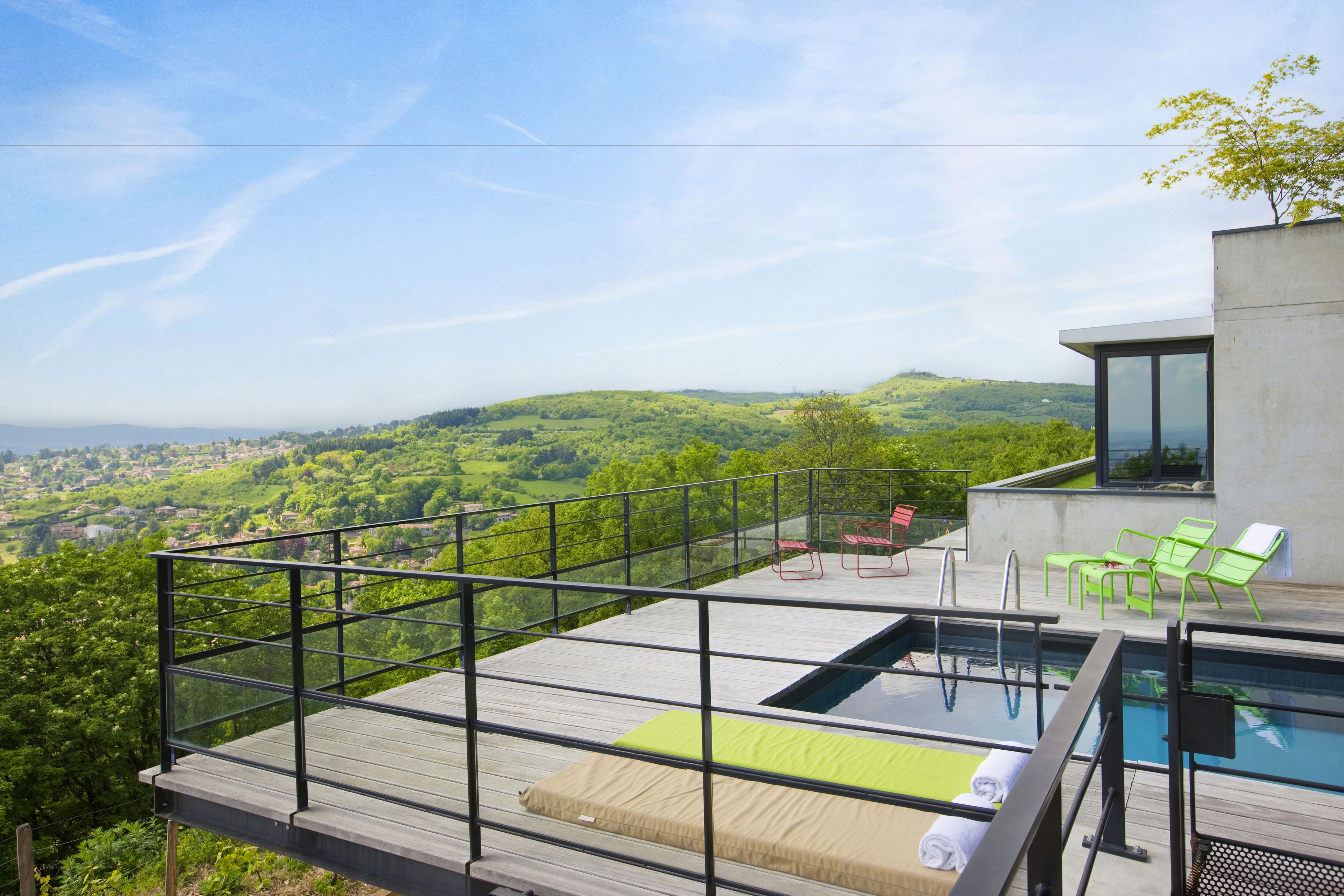 Ein Pool auf dem Dach mit Glasbrüstung, grünen Liegestühlen und Blick auf ein üppiges Tal.