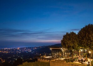 A rooftop terrace with outdoor seating, overlooking a cityscape at dusk.