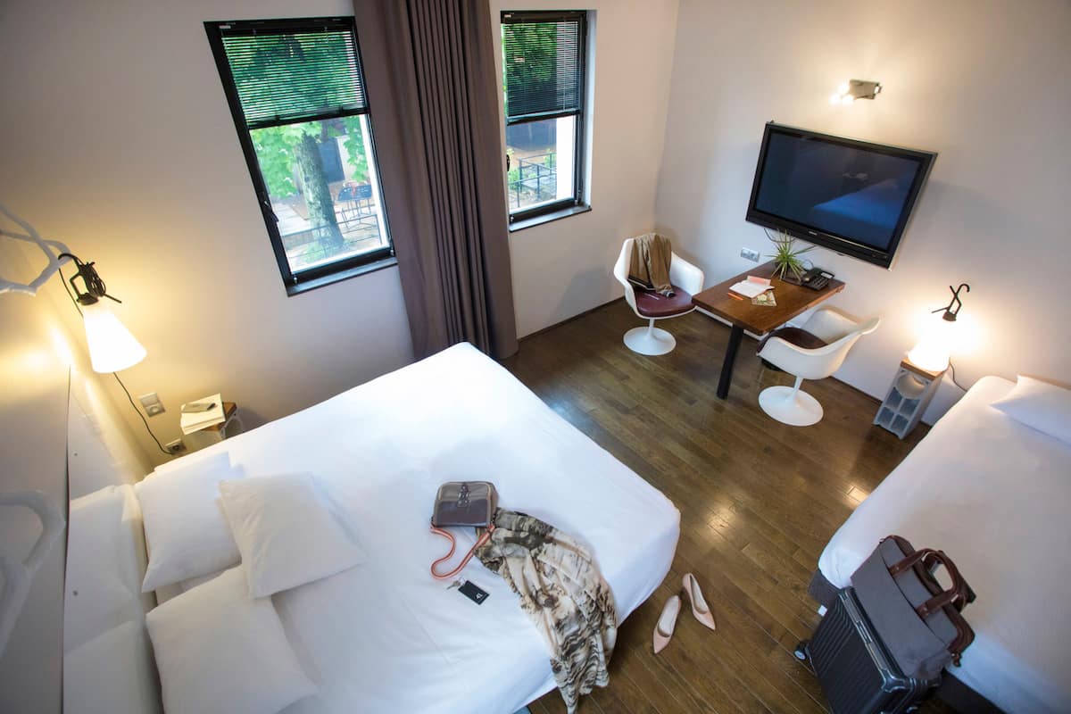 A hotel room with a bed, a desk with a chair, a television, and a window with curtains.