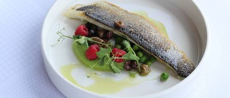 A white plate with a fish, greens, and berries.