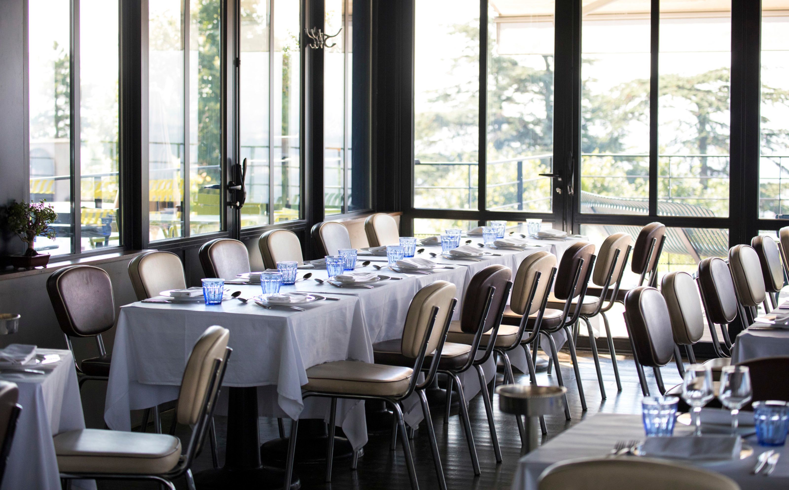 A dining area with tables set for multiple guests, large windows, and a view of the outdoors.